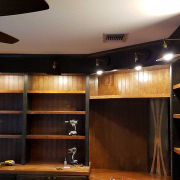 Dark-stained entertainment shelving with track lighting, install in progress