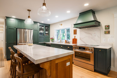 Example of a transitional l-shaped light wood floor and beige floor kitchen design in New York with an undermount sink, shaker cabinets, green cabinets, white backsplash, stone slab backsplash, stainless steel appliances, an island and white countertops