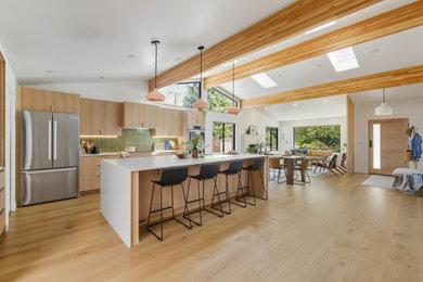Inspiration for a 1960s galley light wood floor, beige floor and exposed beam open concept kitchen remodel in Portland with flat-panel cabinets, light wood cabinets, green backsplash, matchstick tile backsplash, stainless steel appliances, an island and white countertops