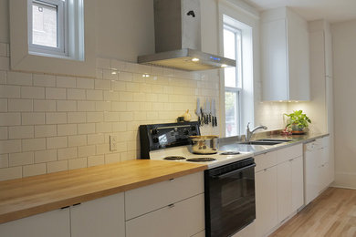 Trendy light wood floor eat-in kitchen photo in Montreal with an integrated sink, flat-panel cabinets, white cabinets, stainless steel countertops, white backsplash, ceramic backsplash and an island