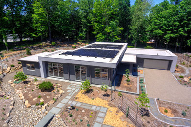 This is an example of a mid-sized modern one-storey grey house exterior in New York with a flat roof and a white roof.