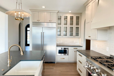 Inspiration for a large timeless l-shaped open concept kitchen remodel in Other with a farmhouse sink, flat-panel cabinets, beige cabinets, quartz countertops, beige backsplash, ceramic backsplash, stainless steel appliances, an island and black countertops