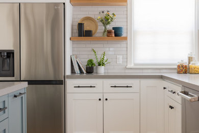 Example of a mid-sized beach style l-shaped medium tone wood floor and brown floor eat-in kitchen design in Los Angeles with shaker cabinets, white cabinets, quartzite countertops, white backsplash, ceramic backsplash, stainless steel appliances, an island and gray countertops