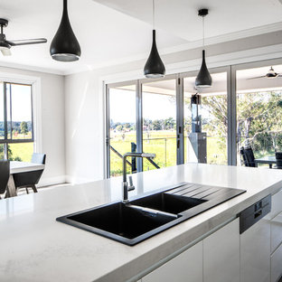 Idéer för att renovera ett stort funkis kök, med en nedsänkt diskho, släta luckor, vita skåp, bänkskiva i kvarts, svart stänkskydd, glaspanel som stänkskydd, rostfria vitvaror, plywoodgolv, en köksö och grått golv