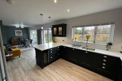 Mid-sized traditional u-shaped open plan kitchen in Other with a double-bowl sink, shaker cabinets, blue cabinets, quartzite benchtops, white splashback, engineered quartz splashback, black appliances, light hardwood floors, brown floor and white benchtop.