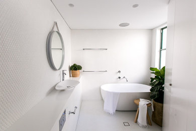This is an example of a mid-sized contemporary bathroom in Sydney with white cabinets, solid surface benchtops, a freestanding tub, a shower/bathtub combo, a wall-mount toilet, white tile, a vessel sink and mosaic tile floors.
