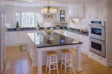 Large elegant u-shaped medium tone wood floor enclosed kitchen photo in Other with an undermount sink, shaker cabinets, white cabinets, granite countertops, white backsplash, ceramic backsplash, stainless steel appliances and an island