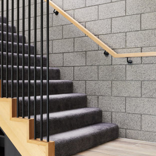 Idée de décoration pour un escalier design en L de taille moyenne avec des marches en moquette, des contremarches en moquette, un garde-corps en bois et un mur en parement de brique.