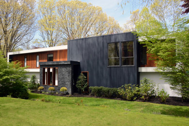 Photo of a mid-sized modern one-storey multi-coloured house exterior in New York with wood siding, a flat roof, a mixed roof, a white roof and board and batten siding.
