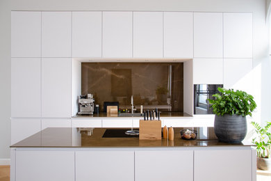 Offene, Zweizeilige, Große Moderne Küche mit integriertem Waschbecken, weißen Schränken, Küchenrückwand in Braun, Küchengeräten aus Edelstahl, braunem Holzboden, Kücheninsel, braunem Boden und brauner Arbeitsplatte in Köln