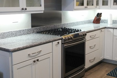 Example of a small transitional l-shaped ceramic tile enclosed kitchen design in Other with shaker cabinets, white cabinets, solid surface countertops, gray backsplash, stainless steel appliances and no island
