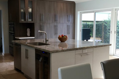 Kitchen - large contemporary travertine floor kitchen idea in Miami with an undermount sink, flat-panel cabinets, light wood cabinets, granite countertops, blue backsplash, glass tile backsplash, stainless steel appliances and an island