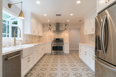 Example of an arts and crafts cement tile floor and beige floor kitchen design in Los Angeles with a farmhouse sink, shaker cabinets, white cabinets, white backsplash, stainless steel appliances and white countertops