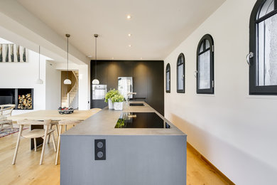 Large modern single-wall open plan kitchen in Paris with concrete benchtops, light hardwood floors and grey benchtop.