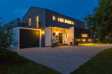 Large contemporary two-storey grey house exterior in Munich with wood siding, a gable roof and a tile roof.