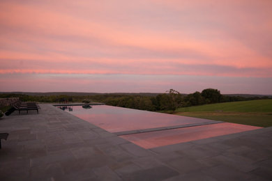 This is an example of a large country backyard rectangular infinity pool in New York with natural stone pavers.