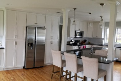 Large transitional l-shaped light wood floor and brown floor eat-in kitchen photo in Other with an undermount sink, shaker cabinets, white cabinets, granite countertops, white backsplash, subway tile backsplash, stainless steel appliances and an island