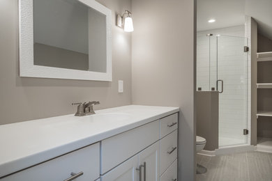 Corner shower - mid-sized transitional 3/4 gray tile and ceramic tile ceramic tile corner shower idea in Kansas City with shaker cabinets, white cabinets, a two-piece toilet, beige walls, solid surface countertops and an integrated sink