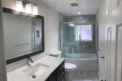 Example of a mid-sized trendy kids' porcelain tile, gray floor and single-sink drop-in bathtub design in Toronto with flat-panel cabinets, brown cabinets, a one-piece toilet, white walls, a drop-in sink, quartz countertops, white countertops, a niche and a built-in vanity