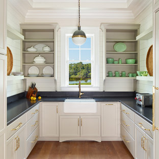На фото: класса люкс большие п-образные кухни в классическом стиле с раковиной в стиле кантри, белым фартуком, паркетным полом среднего тона, кладовкой, фасадами в стиле шейкер, бежевыми фасадами, столешницей из гранита, фартуком из дерева, техникой под мебельный фасад и коричневым полом без острова