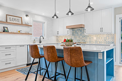 Ejemplo de cocina contemporánea de tamaño medio con armarios estilo shaker, puertas de armario azules, salpicadero azul, suelo de madera clara, una isla y encimeras blancas
