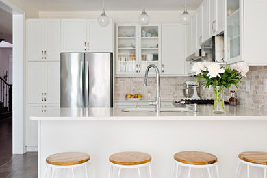 Elegant u-shaped brown floor eat-in kitchen photo in Toronto with an undermount sink, shaker cabinets, white cabinets, beige backsplash, stainless steel appliances, a peninsula and white countertops