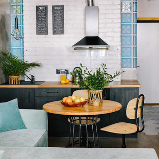 Imagen de cocina lineal, industrial, pequeña, abierta, con fregadero encastrado, armarios con paneles lisos, puertas de armario negras, encimera de madera, salpicadero blanco, suelo de madera en tonos medios, suelo marrón y encimeras marrones