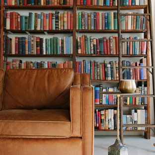 Immagine di un piccolo soggiorno industriale stile loft con libreria, pareti bianche, pavimento in cemento, nessun camino, TV nascosta e pavimento bianco