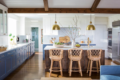 Inspiration for a large coastal u-shaped medium tone wood floor, brown floor and exposed beam open concept kitchen remodel in Los Angeles with an undermount sink, beaded inset cabinets, blue cabinets, marble countertops, white backsplash, marble backsplash, stainless steel appliances, an island and white countertops