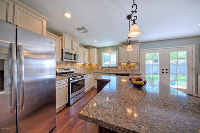 Example of a large classic l-shaped medium tone wood floor open concept kitchen design in Phoenix with an undermount sink, recessed-panel cabinets, beige cabinets, granite countertops, beige backsplash, stone tile backsplash, stainless steel appliances and an island
