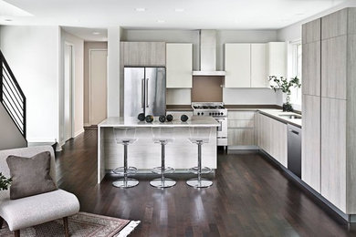 Large trendy l-shaped dark wood floor open concept kitchen photo in Detroit with an undermount sink, flat-panel cabinets, beige cabinets, quartzite countertops, beige backsplash, stone slab backsplash, stainless steel appliances and an island
