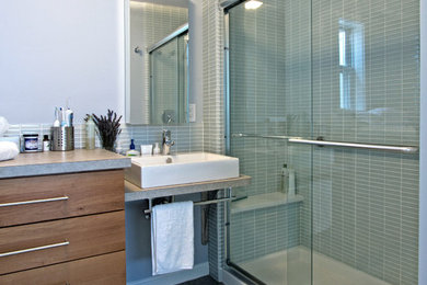 Photo of a mid-sized contemporary bathroom in DC Metro with a vessel sink, flat-panel cabinets, laminate benchtops, an alcove shower, a one-piece toilet, gray tile, glass tile, grey walls, porcelain floors and medium wood cabinets.