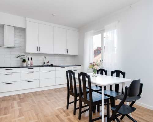 Inredning av ett skandinaviskt mellanstort linjärt kök och matrum, med släta luckor, vita skåp, vitt stänkskydd, stänkskydd i tunnelbanekakel och ljust trägolv