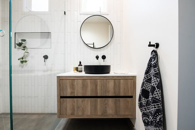 Design ideas for a mid-sized contemporary master bathroom in Melbourne with furniture-like cabinets, medium wood cabinets, a corner shower, white tile, ceramic tile, white walls, porcelain floors, a vessel sink, engineered quartz benchtops, brown floor, a hinged shower door and white benchtops.