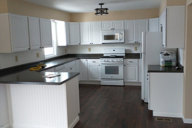 Kitchen - large contemporary u-shaped medium tone wood floor and brown floor kitchen idea in Columbus with an undermount sink, raised-panel cabinets, white cabinets, laminate countertops, black backsplash, shiplap backsplash, white appliances, a peninsula and black countertops