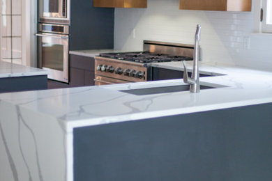 Example of a mid-sized 1960s l-shaped medium tone wood floor eat-in kitchen design in St Louis with an undermount sink, flat-panel cabinets, medium tone wood cabinets, quartz countertops, white backsplash, subway tile backsplash, stainless steel appliances, a peninsula and white countertops