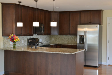 Small elegant u-shaped light wood floor and brown floor open concept kitchen photo in Other with a double-bowl sink, flat-panel cabinets, medium tone wood cabinets, granite countertops, beige backsplash, glass tile backsplash, stainless steel appliances and a peninsula