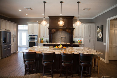 Example of a transitional dark wood floor open concept kitchen design in Tampa with a farmhouse sink, raised-panel cabinets, white cabinets, granite countertops, gray backsplash, subway tile backsplash, stainless steel appliances and an island