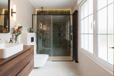 Modelo de cuarto de baño principal, único y flotante contemporáneo grande con armarios con paneles lisos, puertas de armario de madera en tonos medios, ducha empotrada, sanitario de pared, baldosas y/o azulejos verdes, baldosas y/o azulejos de cerámica, paredes beige, suelo de baldosas de cerámica, lavabo sobreencimera, encimera de laminado, suelo beige, ducha con puerta corredera, encimeras marrones y hornacina