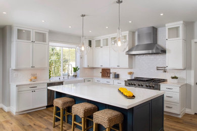 Open concept kitchen - large farmhouse u-shaped vinyl floor and brown floor open concept kitchen idea with a farmhouse sink, shaker cabinets, white cabinets, quartz countertops, white backsplash, ceramic backsplash, stainless steel appliances, an island and white countertops