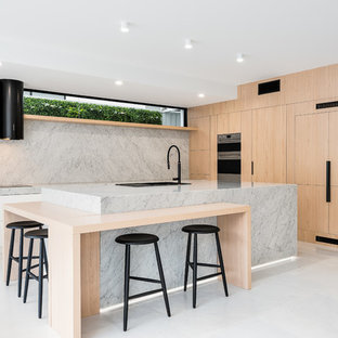 Cette photo montre une grande arrière-cuisine moderne en L avec un évier encastré, un placard à porte affleurante, des portes de placard en bois clair, un plan de travail en marbre, une crédence blanche, une crédence en marbre, un électroménager noir, un sol en marbre, un îlot central, un sol blanc et un plan de travail blanc.