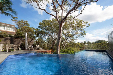 Mid-sized modern backyard custom-shaped infinity pool in Sydney with natural stone pavers.