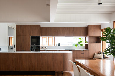 Photo of a mid-sized contemporary galley eat-in kitchen in Brisbane with quartz benchtops, with island, white benchtop, an undermount sink, flat-panel cabinets, medium wood cabinets, window splashback, black appliances, medium hardwood floors and brown floor.