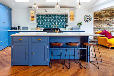 Photo of a medium sized traditional l-shaped kitchen/diner in Berkshire with a built-in sink, shaker cabinets, blue cabinets, quartz worktops, green splashback, porcelain splashback, coloured appliances, vinyl flooring, an island, brown floors and white worktops.