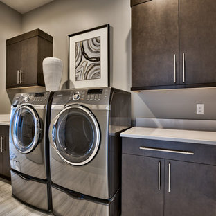 Inspiration for a contemporary l-shaped separated utility room in Omaha with a submerged sink, a side by side washer and dryer, flat-panel cabinets, brown cabinets, grey walls, grey floors and white worktops.
