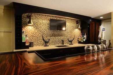 Example of a mid-sized transitional galley dark wood floor and brown floor seated home bar design in New York with an undermount sink, flat-panel cabinets, black cabinets, beige backsplash and stone tile backsplash