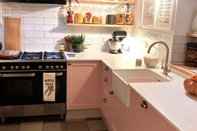 Small bohemian grey and pink u-shaped enclosed kitchen in Other with a belfast sink, shaker cabinets, pink cabinets, quartz worktops, white splashback, metro tiled splashback, black appliances, ceramic flooring, no island, multi-coloured floors, white worktops and exposed beams.
