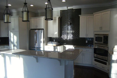 Example of a mid-sized transitional l-shaped dark wood floor open concept kitchen design in New York with an undermount sink, shaker cabinets, white cabinets, granite countertops, black backsplash, subway tile backsplash, stainless steel appliances and an island