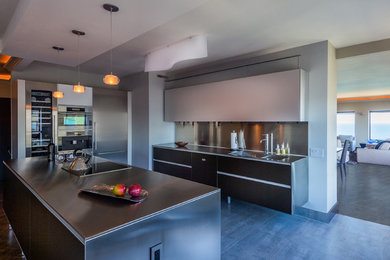 Large modern galley open plan kitchen in Chicago with an integrated sink, raised-panel cabinets, white cabinets, stainless steel benchtops, metallic splashback, stainless steel appliances, ceramic floors and with island.