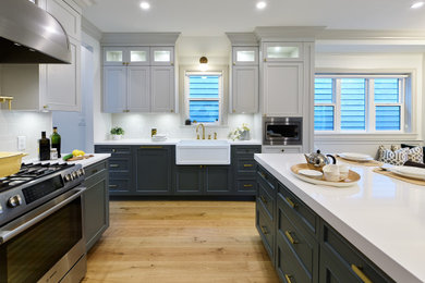 Kitchen - mid-sized modern u-shaped light wood floor and brown floor kitchen idea in Vancouver with a farmhouse sink, blue cabinets, marble countertops, white backsplash, subway tile backsplash, stainless steel appliances, an island and white countertops